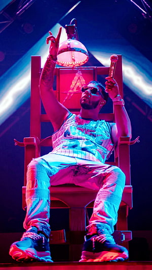 Anuel AA Seated on Stage Throne Under Neon Pink and Blue Concert Lighting HD phone wallpaper