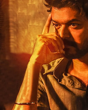 Vijay in a contemplative close-up portrait with warm golden lighting and dramatic shadows HD phone wallpaper