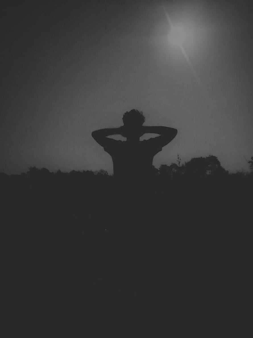 Silhouette of a person with hands behind head against a dark sky with a bright light source HD phone wallpaper