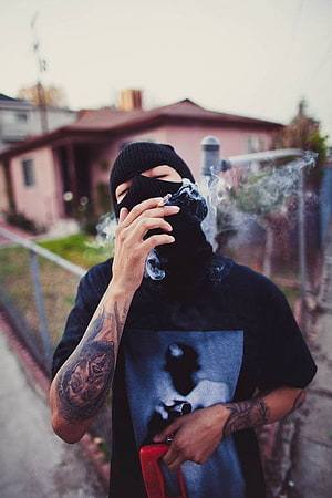 Man in black ski mask smoking cigarette with visible arm tattoos in residential neighborhood HD phone wallpaper