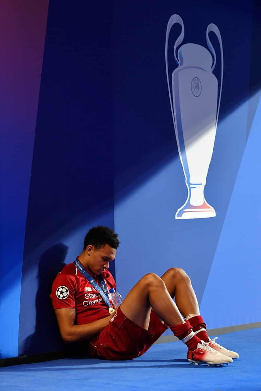 Trent Alexander-Arnold in red Liverpool kit sitting on pitch with Champions League trophy backdrop HD phone wallpaper