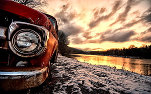 Rusty vintage car parked on a snowy riverbank under a dramatic golden sunset sky HD wallpaper