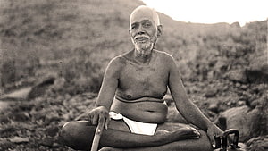 Sri Ramana Maharshi seated in meditation on a rocky hillside in a vintage black and white photograph HD wallpaper