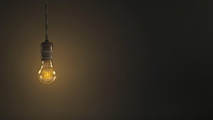 Glowing vintage Edison bulb hanging from a twisted cord against a dark moody background HD wallpaper