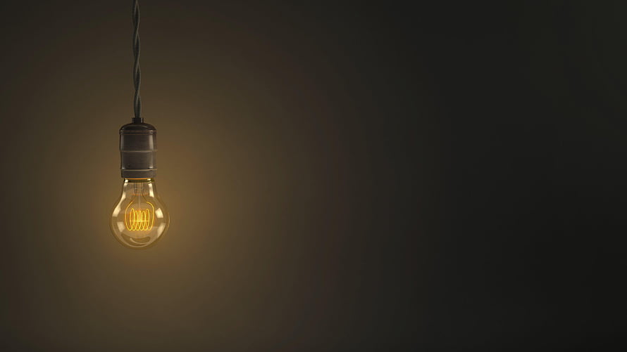 Glowing vintage Edison bulb hanging from a twisted cord against a dark moody background HD wallpaper