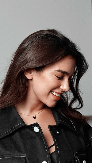 Dua Lipa smiling in profile wearing a black jacket and delicate necklace HD phone wallpaper