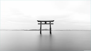 Minimalist Black and White Torii Gate Standing in Calm Water with Distant Mountains HD wallpaper