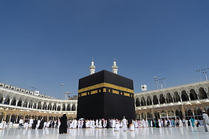 The Kaaba in Mecca with pilgrims gathered in the courtyard under a clear blue sky HD wallpaper