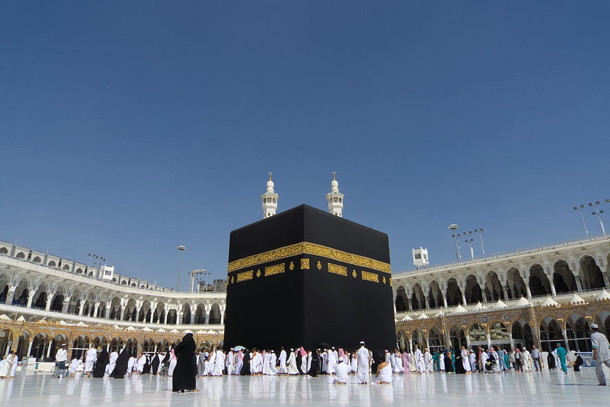 The Kaaba in Mecca with pilgrims gathered in the courtyard under a clear blue sky HD wallpaper