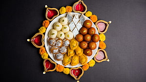 Traditional Indian Mithai Sweets Arranged on a Plate with Diya Lamps and Marigold Flowers for Diwali HD wallpaper
