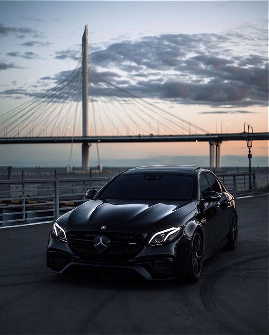 Black Mercedes-AMG E63 S Coupe Parked on a Coastal Road at Dusk with a Cable-Stayed Bridge in the Background HD phone wallpaper
