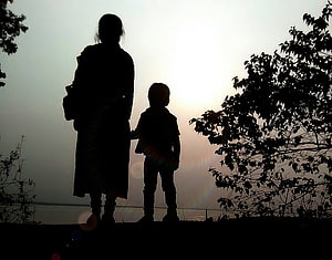 Silhouette of a mother and child standing together at sunset with trees in the background HD wallpaper