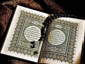 Open Quran with ornate green arabesque borders and black prayer beads on dark fabric HD wallpaper