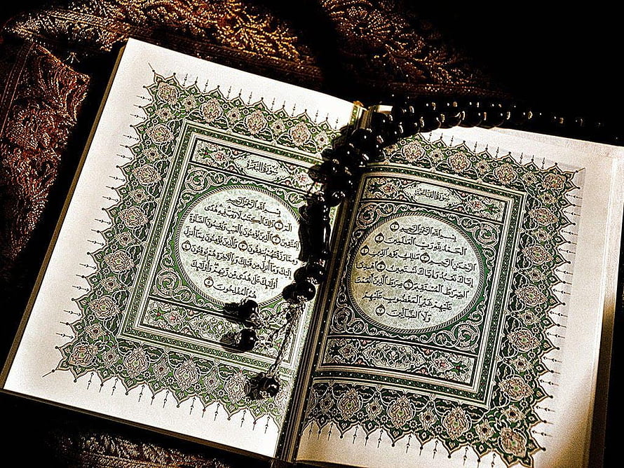 Open Quran with ornate green arabesque borders and black prayer beads on dark fabric HD wallpaper