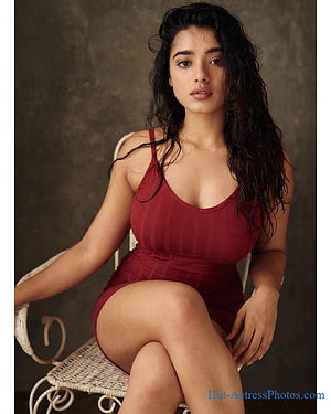 Kethika Sharma in a red bodysuit seated on a wicker chair against a textured studio backdrop HD phone wallpaper