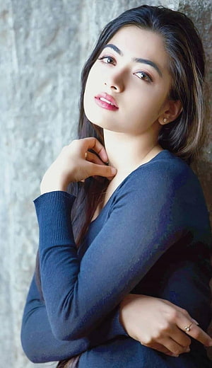 Rashmika Mandanna in a navy blue top with a soft, contemplative expression against a textured wall HD phone wallpaper