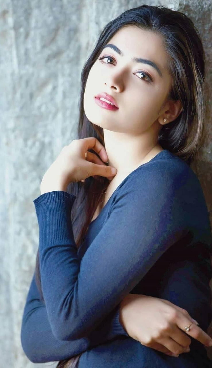 Rashmika Mandanna in a navy blue top with a soft, contemplative expression against a textured wall HD phone wallpaper