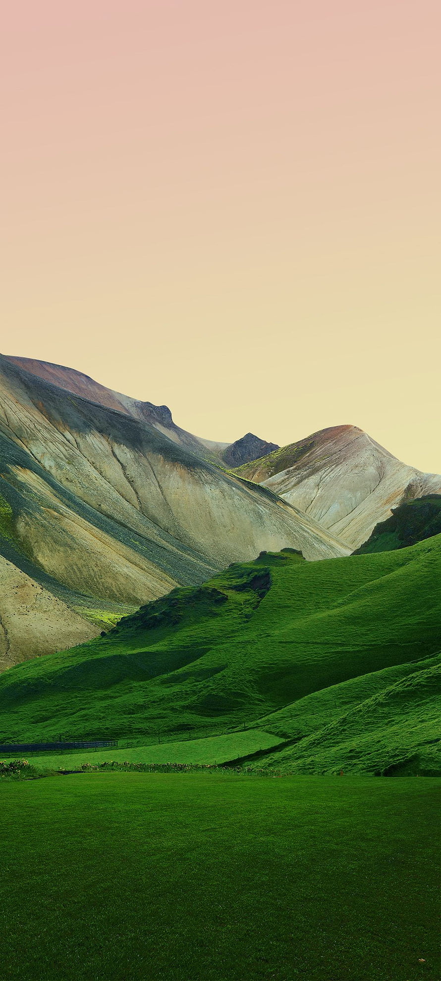 Lush Green Rolling Hills and Arid Mountain Slopes Under a Soft Pastel Sky HD phone wallpaper