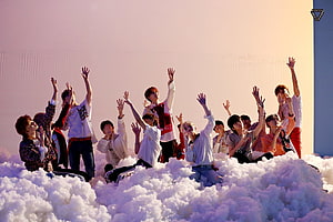 Seventeen members posing on a cloud set with raised hands in a pastel-toned studio HD wallpaper