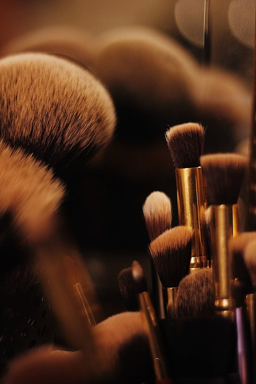 Close-up of soft brown makeup brushes with gold ferrules arranged in a warm, moody setting HD phone wallpaper