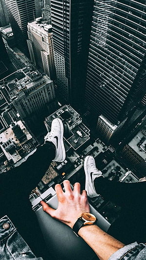 First-person view of white sneakers dangling over a dense city skyline from a high-rise ledge HD phone wallpaper