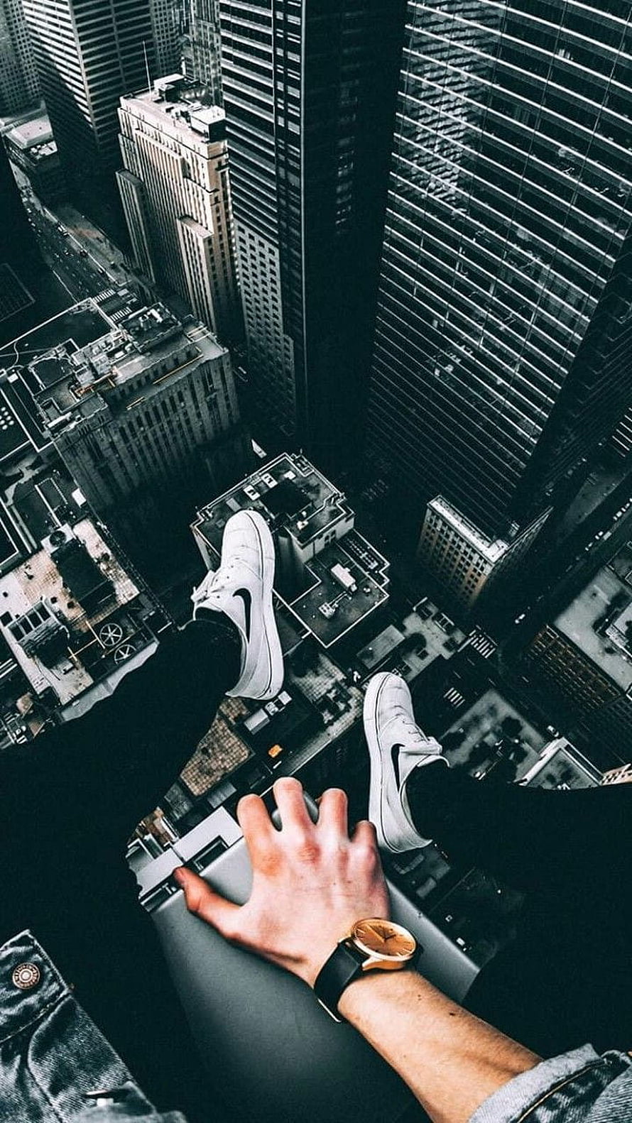 First-person view of white sneakers dangling over a dense city skyline from a high-rise ledge HD phone wallpaper