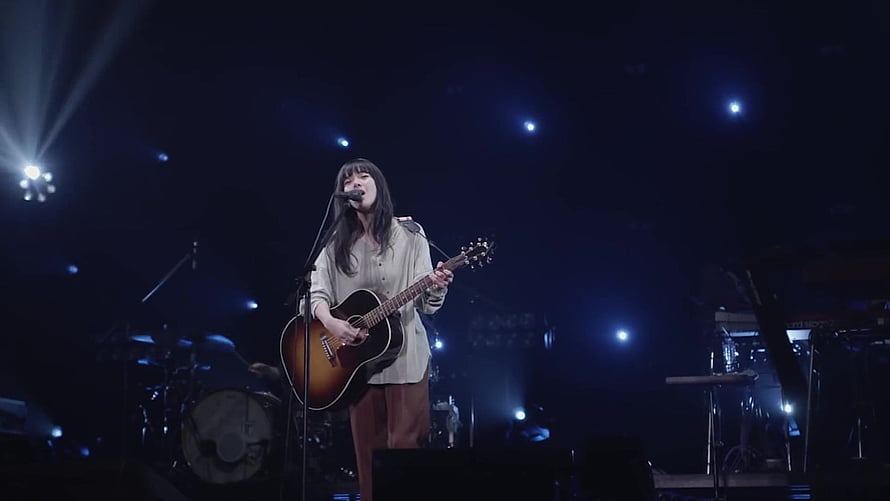 Aimyon performing live on stage with acoustic guitar under blue concert lighting HD wallpaper