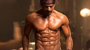 Shah Rukh Khan shirtless with defined abs and headband in dramatic warm lighting HD wallpaper