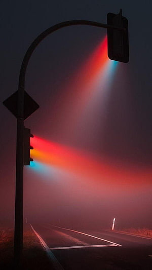 Glowing traffic signal casting red and blue light beams through dense fog on a dark road HD phone wallpaper