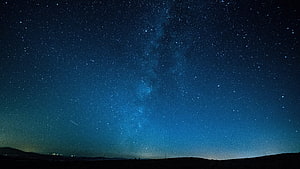 Milky Way Galaxy Arching Over a Dark Horizon Under a Deep Blue Starry Night Sky HD wallpaper