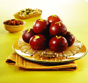 Glossy Gulab Jamun Sweets with Pistachio Garnish on a Glass Plate HD wallpaper