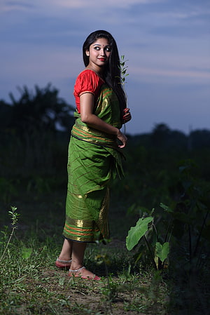 Bengali woman in green silk saree and red blouse standing in a rural field at dusk HD phone wallpaper