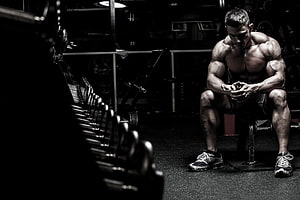 Muscular Athlete Resting on Gym Bench in Dark Fitness Studio HD wallpaper