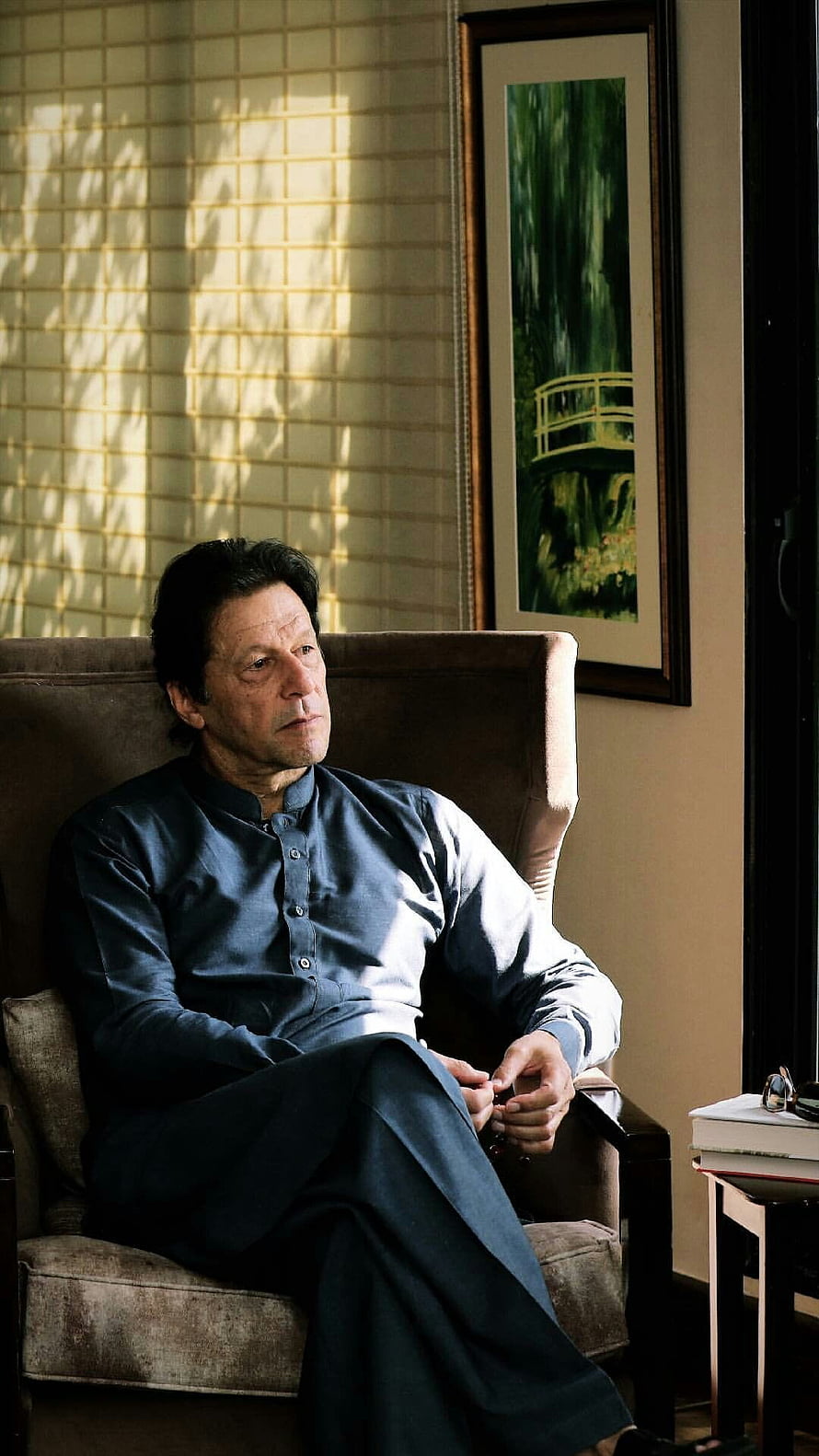 Imran Khan seated in a contemplative pose wearing a dark blue shalwar kameez in a warmly lit interior HD phone wallpaper