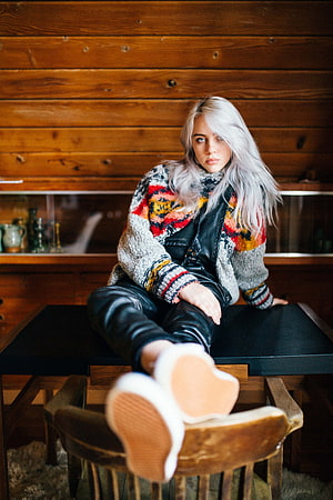 Billie Eilish in Colorful Knit Cardigan and Leather Jacket Seated in Rustic Wooden Interior HD phone wallpaper