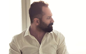 Fahadh Faasil in a white shirt looking out a window with a contemplative expression HD wallpaper