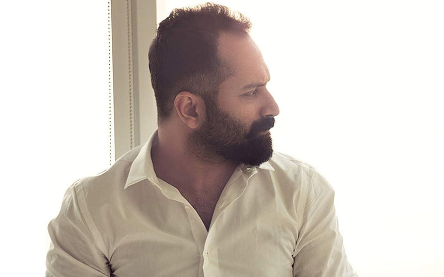 Fahadh Faasil in a white shirt looking out a window with a contemplative expression HD wallpaper