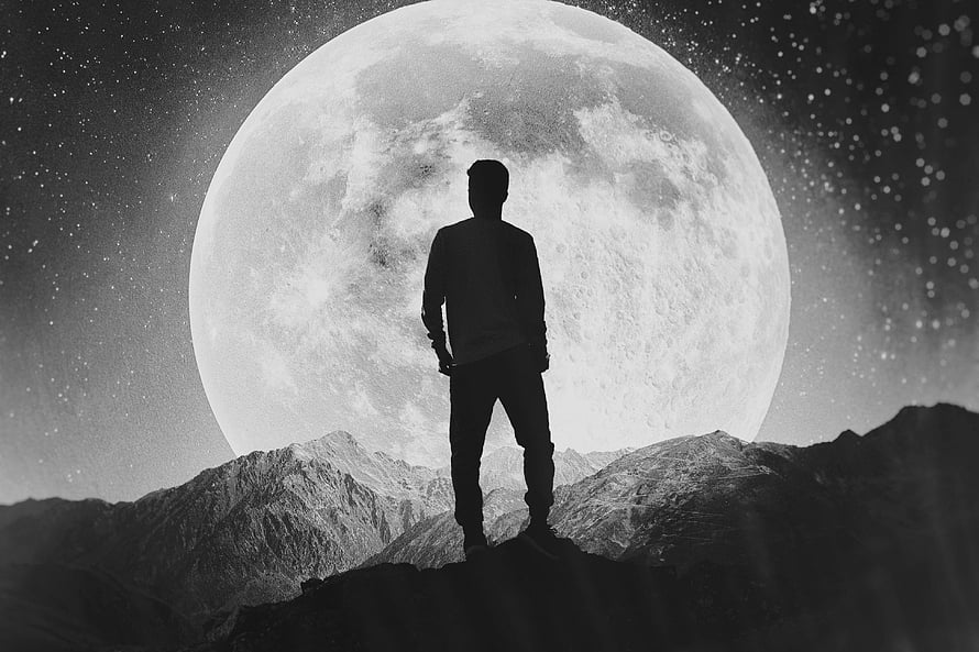 Silhouette of a man standing on a mountain peak beneath a massive full moon in a starry night sky HD wallpaper