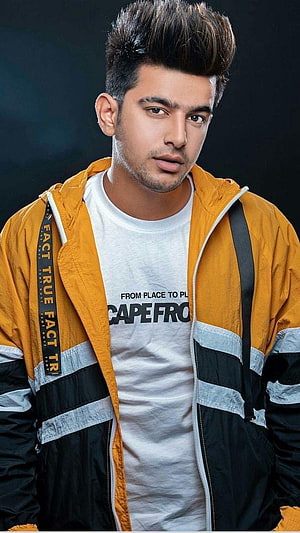 Jass Manak in a yellow and black jacket with a white graphic t-shirt against a dark studio background HD phone wallpaper