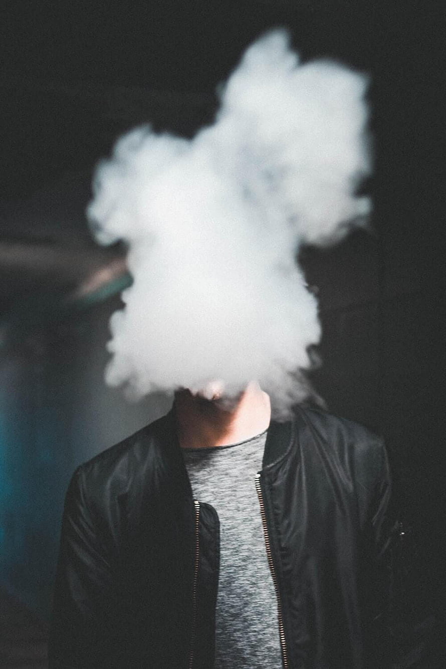 Man in black bomber jacket exhaling thick white smoke against dark background HD phone wallpaper