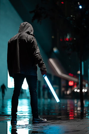 Hooded Figure Holding Blue Light Sword on Rainy Night Street HD phone wallpaper