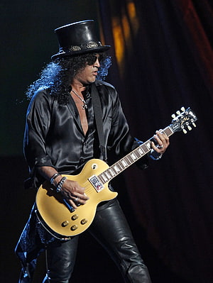 Slash performing live on stage in a black top hat and satin shirt with a gold Gibson Les Paul guitar HD phone wallpaper