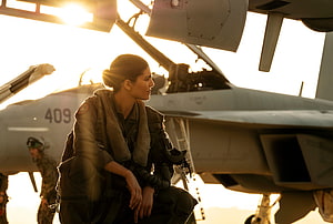 Top Gun Maverick Female Pilot in Flight Suit Seated Before F-18 Jet at Golden Hour HD wallpaper
