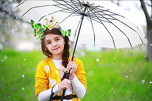 Young girl in yellow cardigan holding white umbrella with butterfly headpiece in a green park HD wallpaper