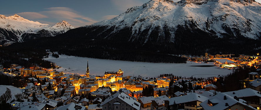 Illuminated Swiss Alpine Village at Dusk with Frozen Lake and Snow-Capped Mountains HD wallpaper