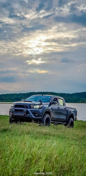 Black Toyota Hilux pickup truck parked in a grassy field near a lake at sunset HD phone wallpaper