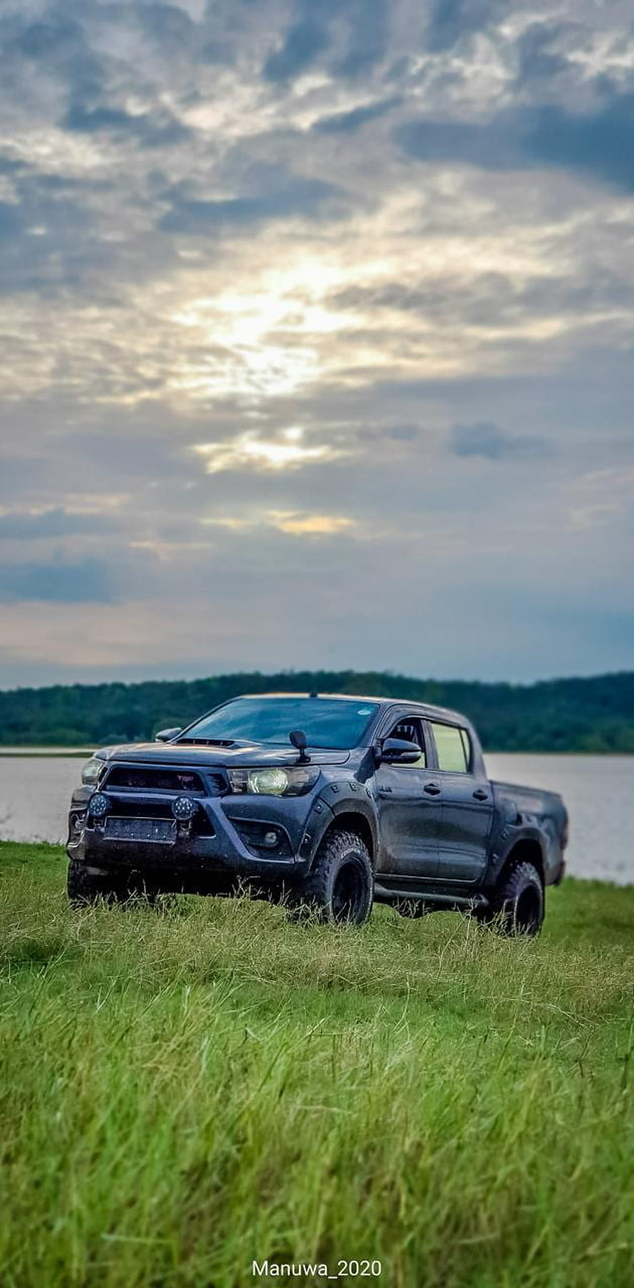 Black Toyota Hilux pickup truck parked in a grassy field near a lake at sunset HD phone wallpaper