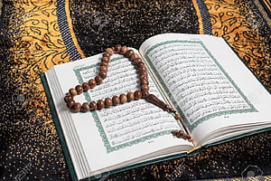 Open Quran with wooden prayer beads resting on ornate prayer mat HD wallpaper