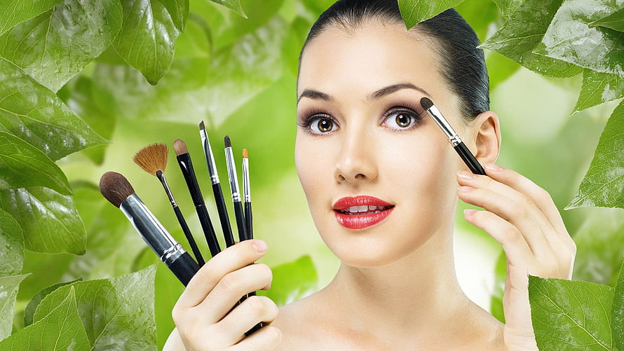 Woman Applying Eye Makeup With Brushes Surrounded By Fresh Green Leaves HD wallpaper