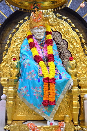 Sai Baba of Shirdi seated on ornate golden throne with vibrant floral garlands and traditional blue attire HD phone wallpaper